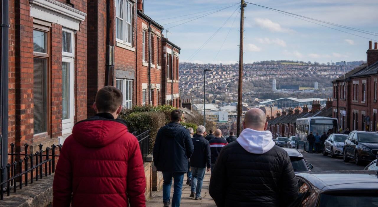 Supporters walking a matchday street with the Sheffield hills behind.